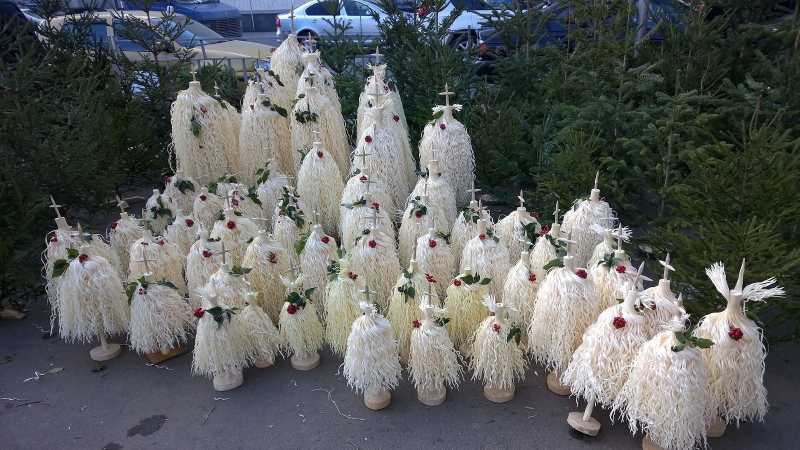 Rows of white chichilaki, shaved-branch Georgian Christmas trees, for sale on a Tbilisi sidewalk beside fir trees