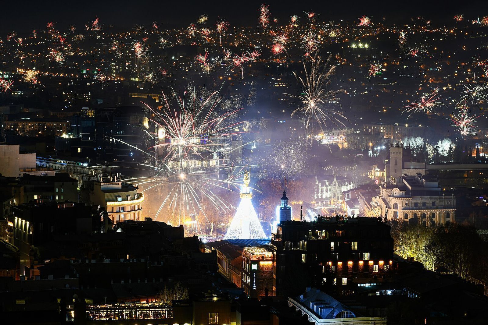 New Year 2026 fireworks over Tbilisi seen from the Sololaki ridge, with the lit tree on Freedom Square below