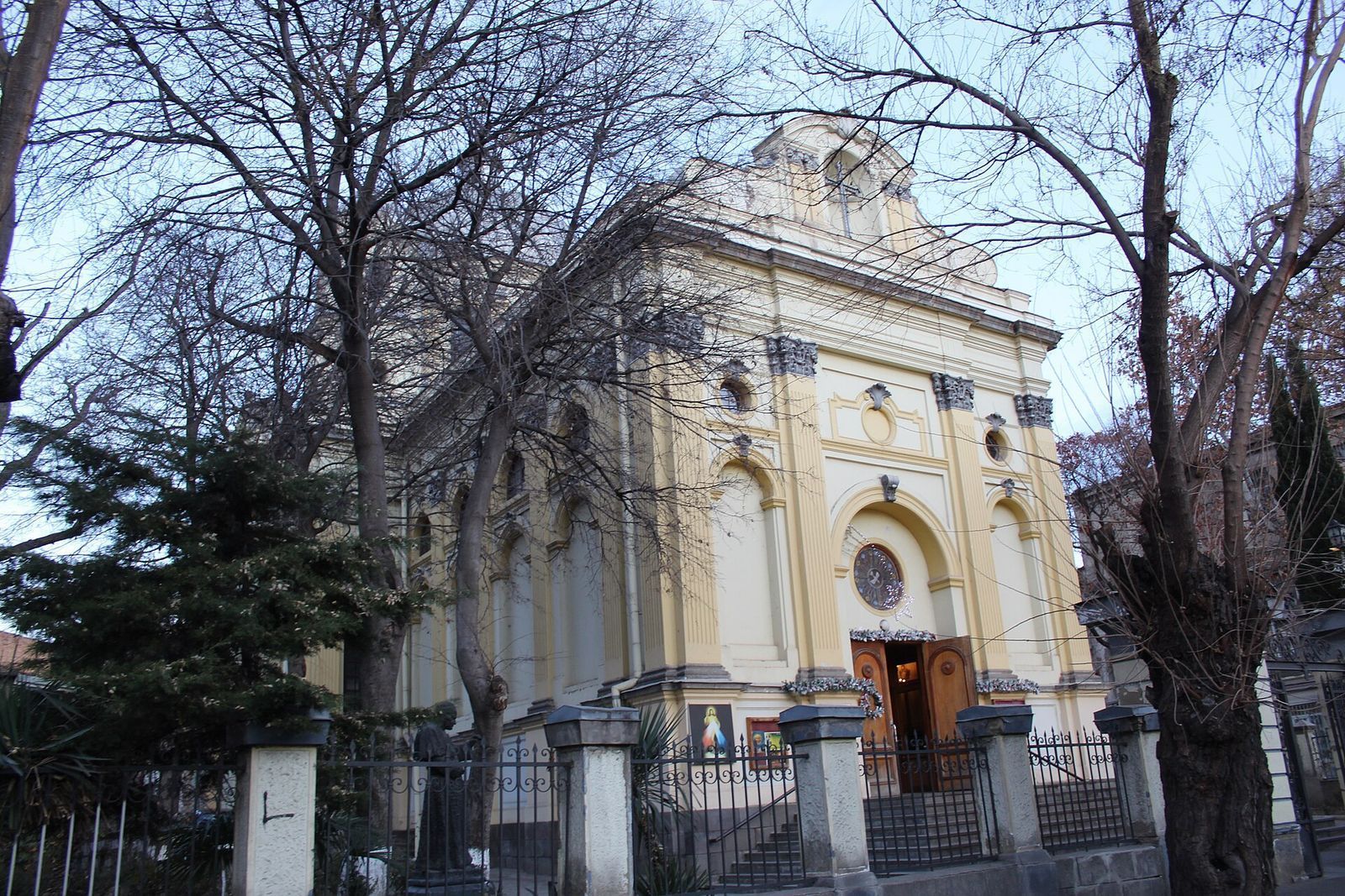 The yellow facade of the Catholic Church of Sts Peter and Paul in Tbilisi in winter, with holiday garlands over the open door