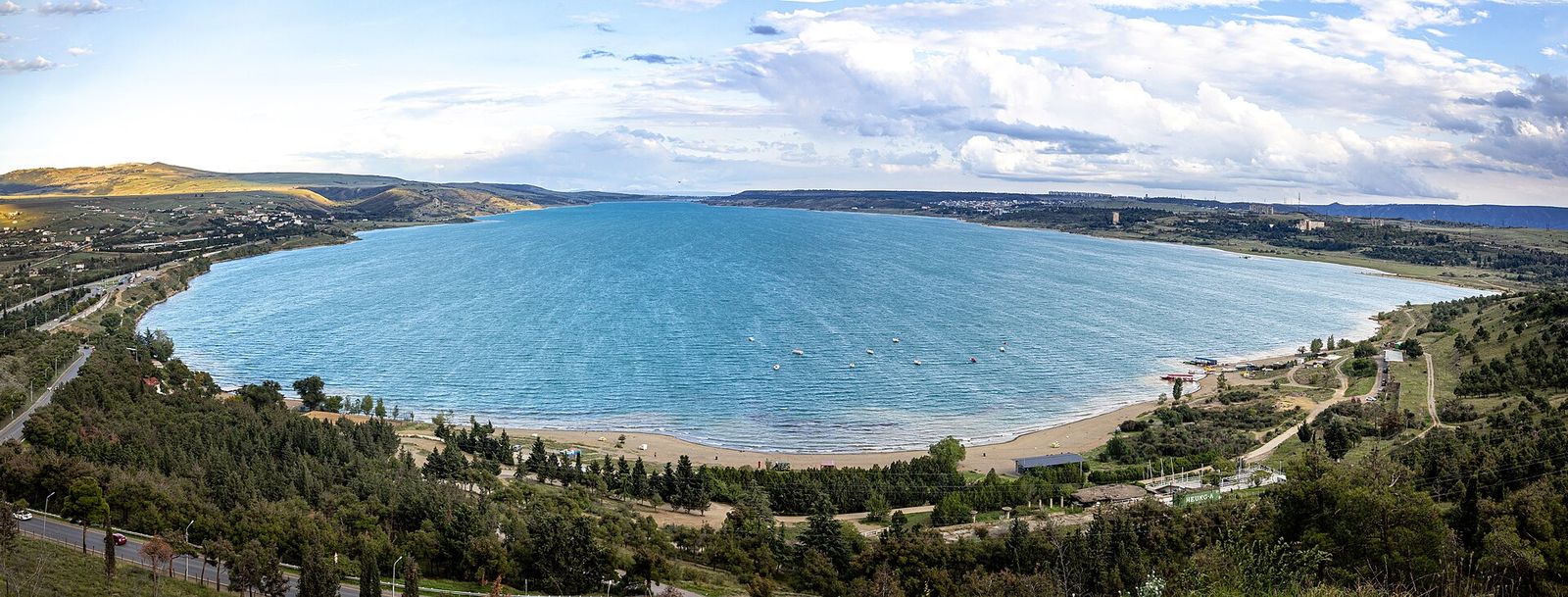The sandy beach on the Tbilisi Sea shore below the Chronicles of Georgia, seen from the monument, with small boats moored offshore