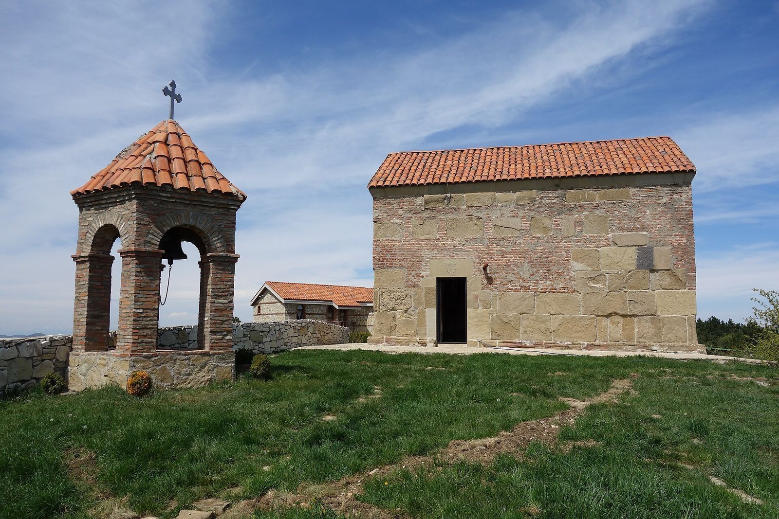 The small stone church and brick bell tower of Udzo Monastery on its grassy hilltop