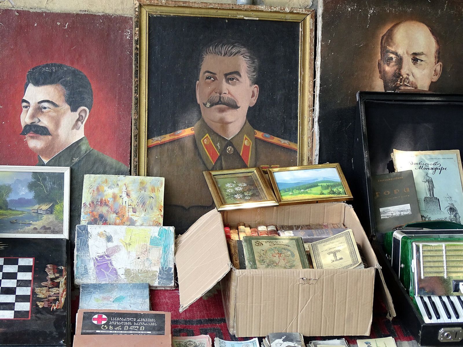Painted portraits of Stalin and Lenin above boxes of small paintings and old postcards at a Tbilisi memorabilia stall