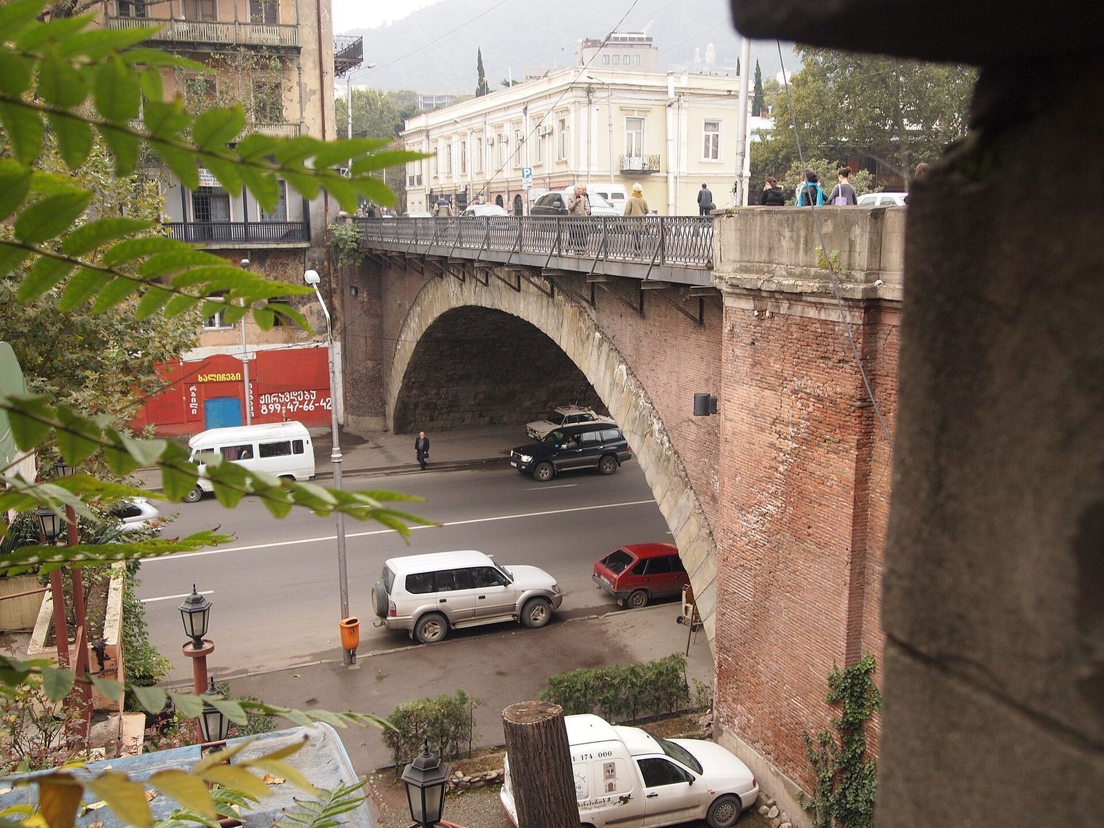 The stone and brick arch of the Dry Bridge in Tbilisi spanning the embankment road, with people walking across the top