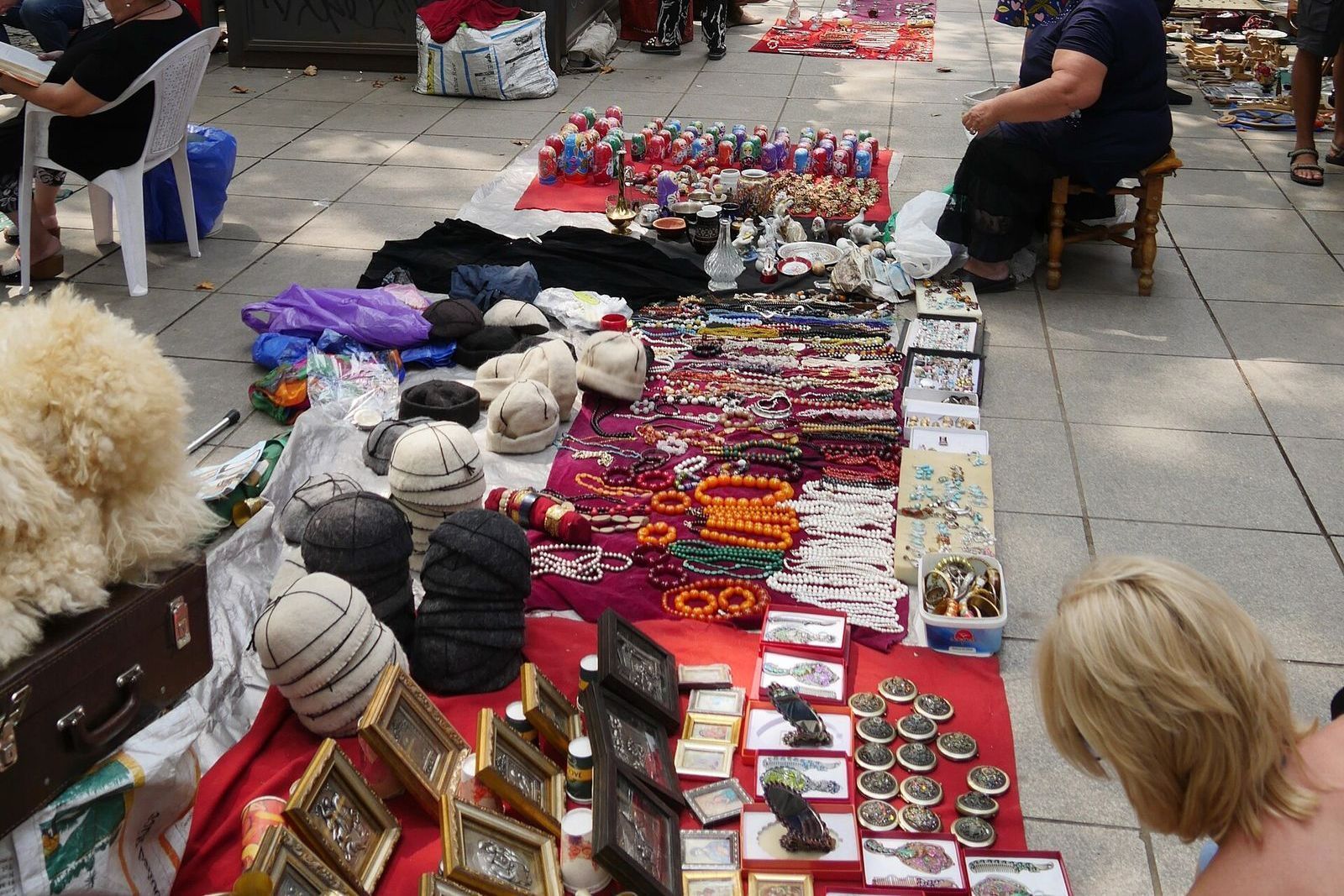 Strings of orange amber-style beads, pearls and coral, with rings and brooches, laid out on a cloth at a Dry Bridge Market jewelry stall