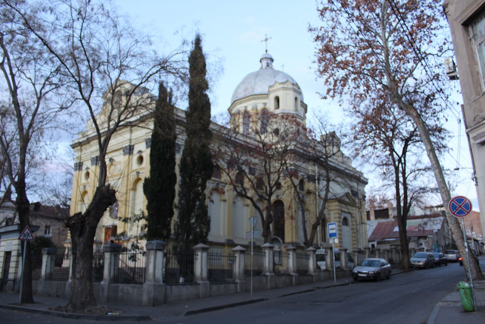 The yellow Catholic church of Sts Peter and Paul in Tbilisi, with its white dome, behind a railing on a quiet street