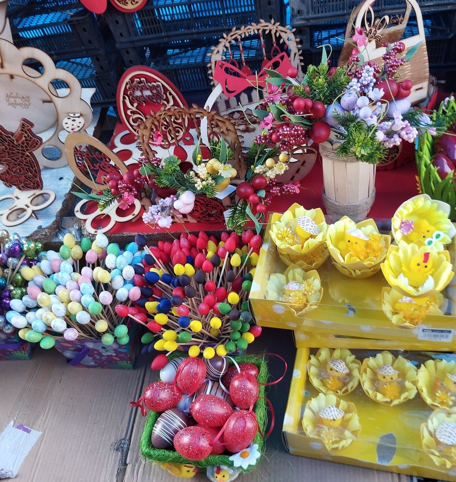 An Easter stall in Georgia set out on cardboard: foam eggs on sticks, glittery red hanging eggs, wooden egg stands and toy chicks
