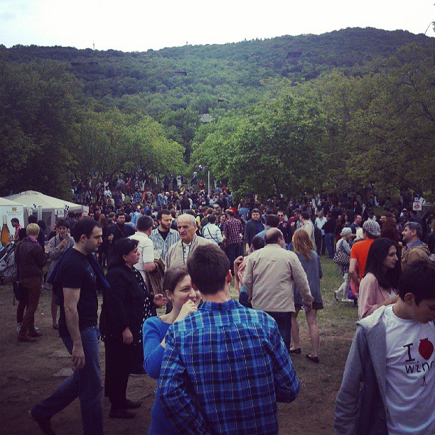 A crowd of visitors among the white tasting tents at the New Wine Festival in Tbilisi in May 2013, with a wooded hillside behind