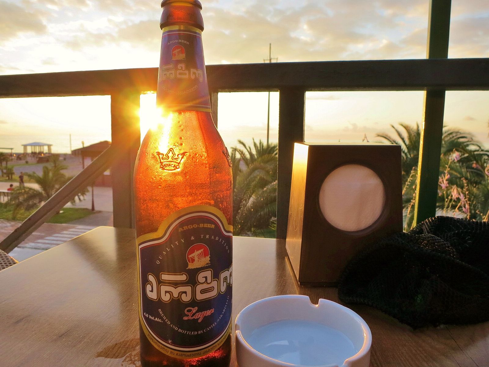 A cold bottle of Argo lager on a balcony table at sunset with palm trees and the Black Sea behind