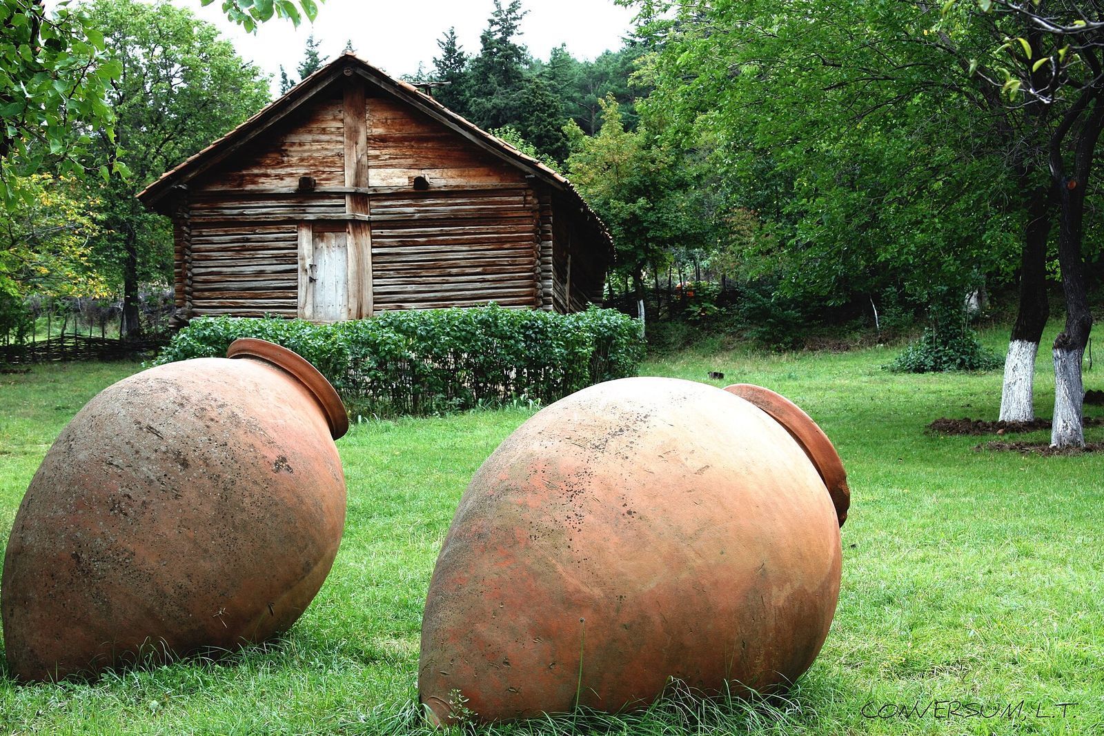 Two large clay qvevri wine jars lying on the grass in front of an old wooden farmhouse in Georgia