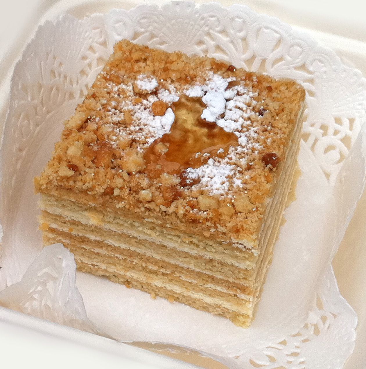 A slice of medoki honey cake showing its thin sponge layers under a crumb and sugar topping