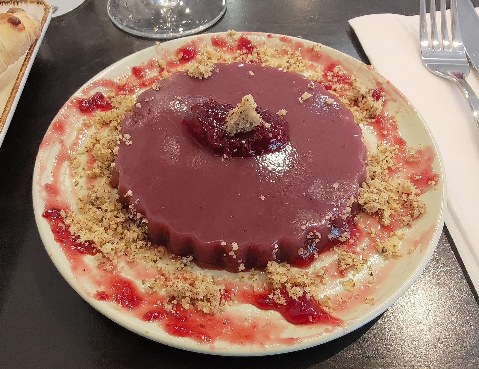 A purple pelamushi grape pudding turned out on a plate, topped with crushed walnuts and fruit jelly