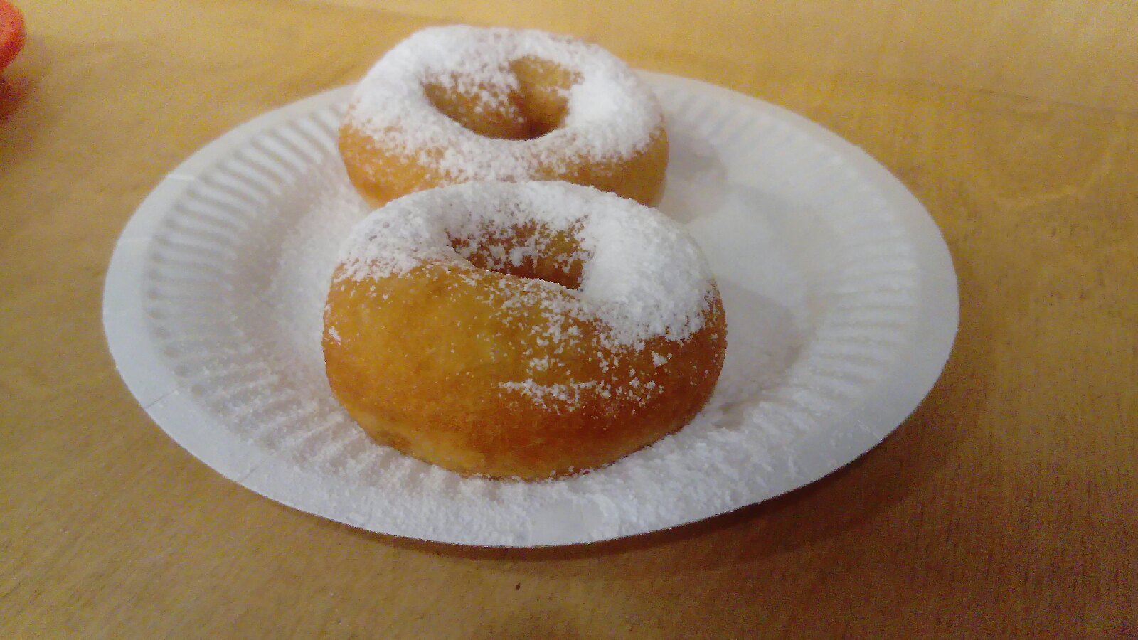 Two pishki ring doughnuts dusted with powdered sugar on a paper plate