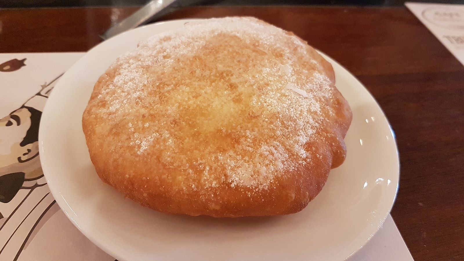 A ponchiki doughnut dusted with sugar on a plate in a Tbilisi cafe