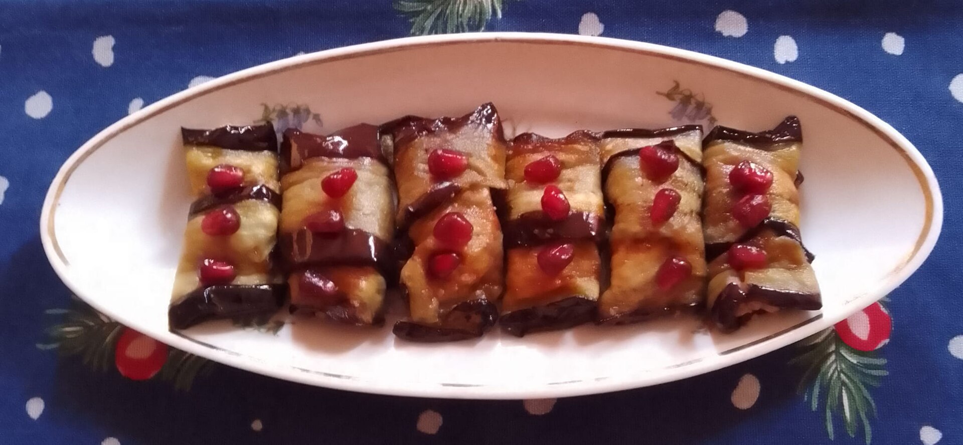 Badrijani nigvzit, fried eggplant slices rolled around walnut paste and dotted with pomegranate seeds, on an oval plate
