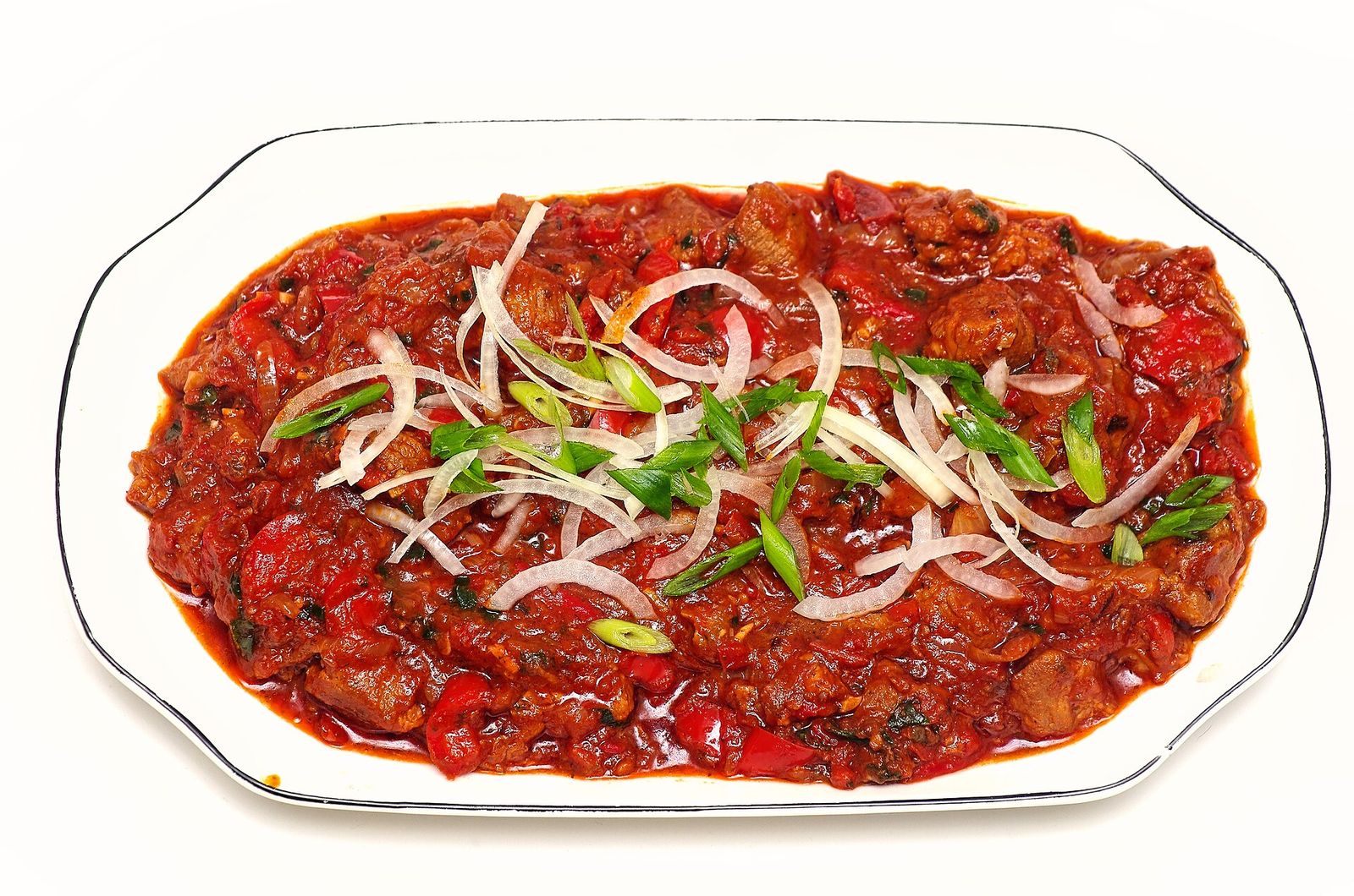 Chashushuli, pieces of meat in a thick tomato and pepper sauce topped with sliced onion and spring onion, on a white platter