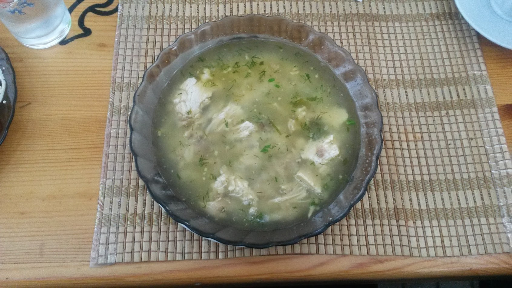 Chikhirtma, a chicken soup thickened with egg, with pieces of chicken and green herbs in a glass bowl