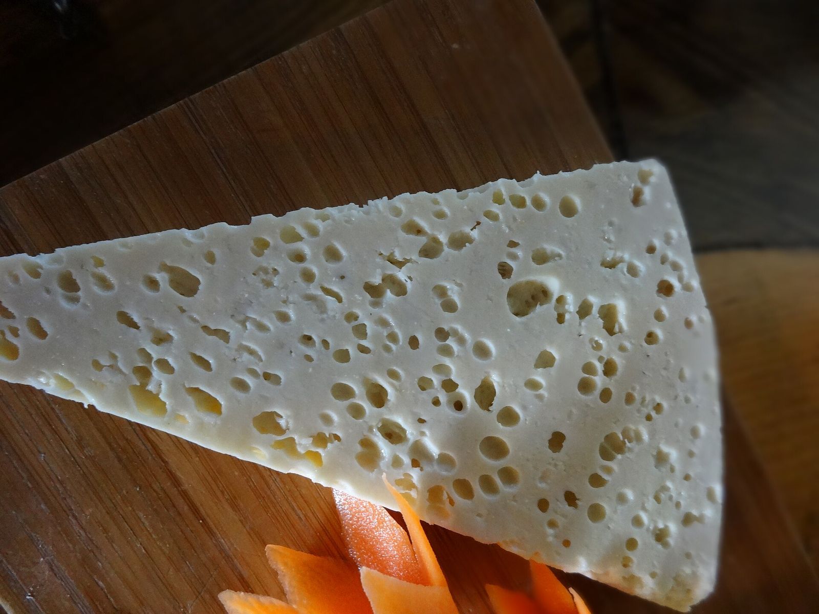 A wedge of guda, a white Georgian sheep's cheese full of small holes, on a wooden board