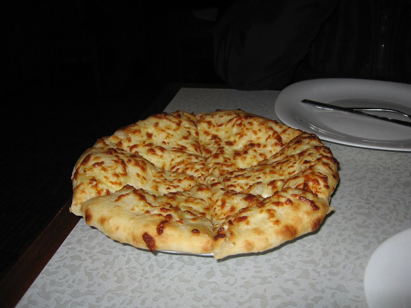 A round Megruli khachapuri with browned cheese baked over the top, cut into slices on a restaurant table