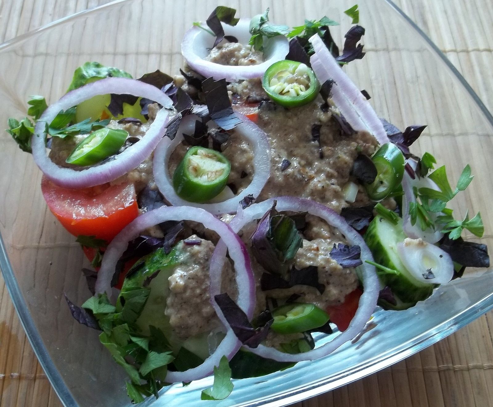 A Georgian salad of tomato, cucumber, red onion, green chili and purple basil with a walnut dressing, in a glass bowl