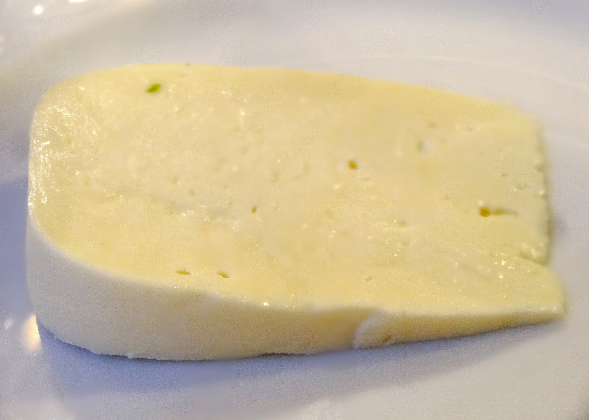 A thick slice of pale yellow sulguni cheese on a white plate