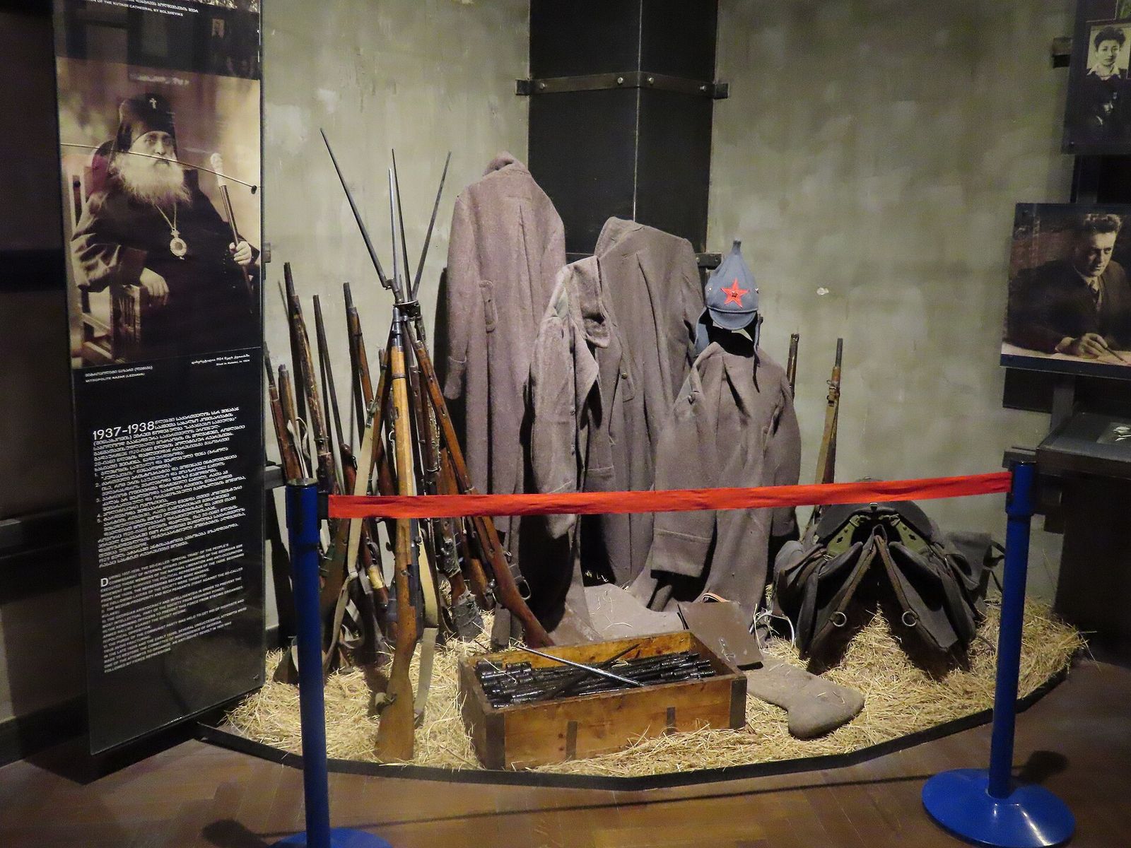 Rifles, greatcoats and an ammunition crate displayed under portraits in the Museum of Soviet Occupation hall in Tbilisi