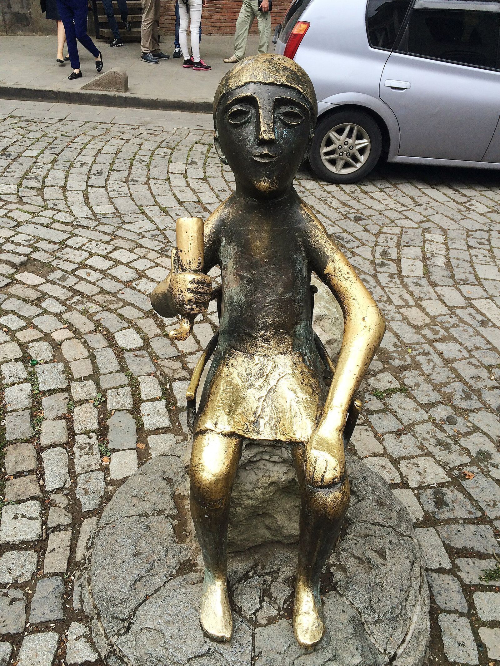 The bronze tamada statue in Tbilisi, a seated toastmaster raising a drinking horn on a cobbled street