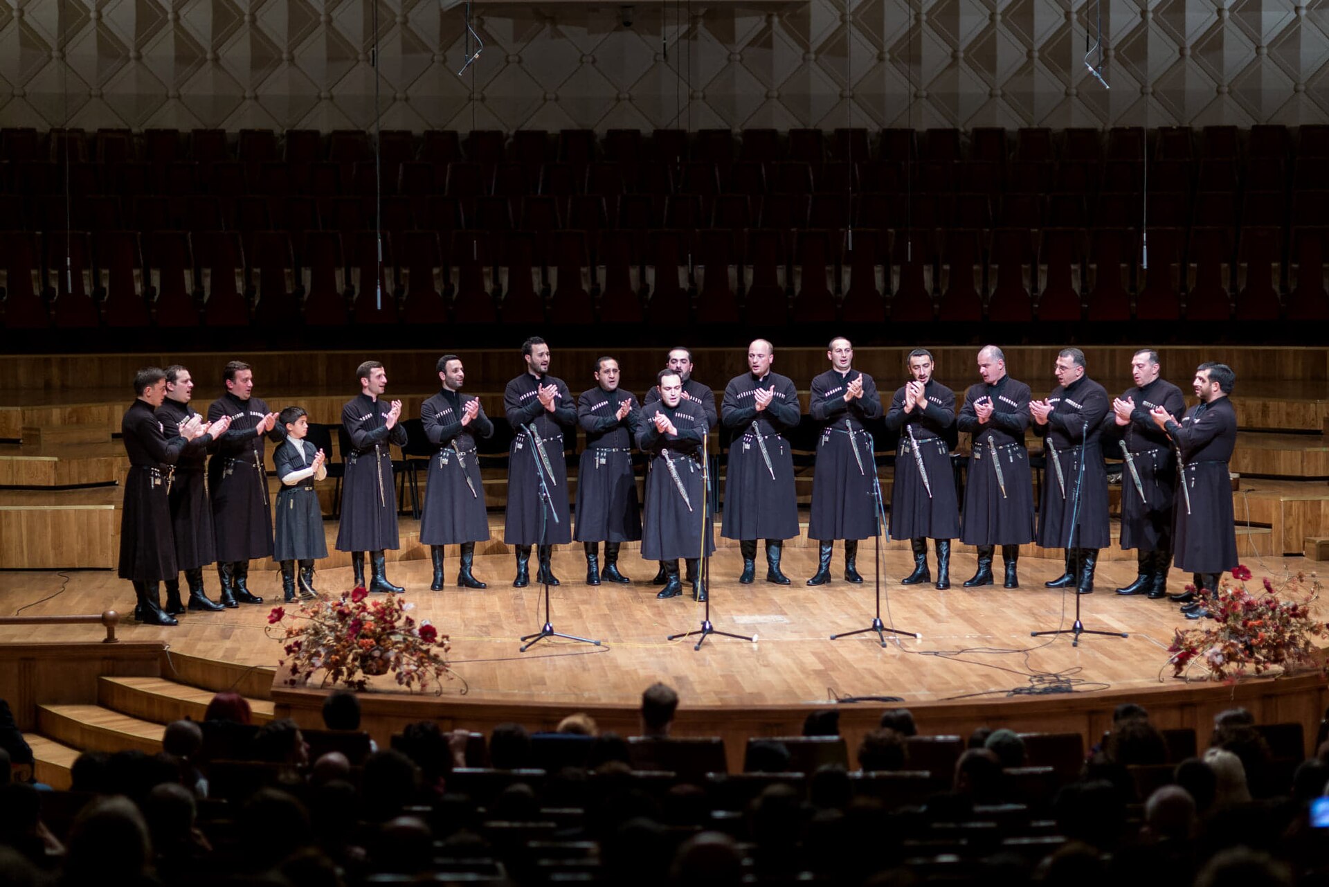 Basiani ensemble in long dark chokhas singing on a concert hall stage