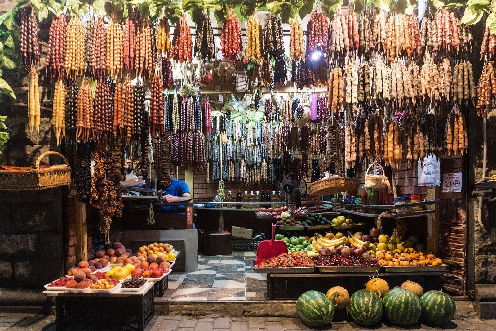 Strings of churchkhela in red, orange and purple hanging above a fruit stall in Tbilisi