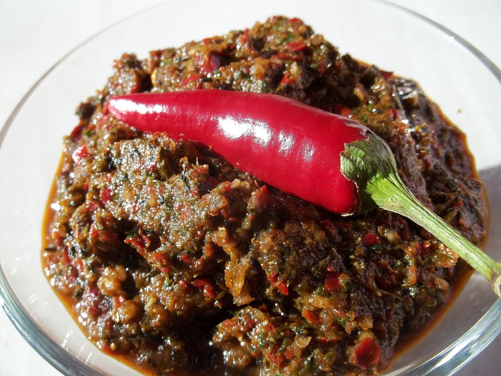 A glass bowl of Megrelian adjika, a coarse paste of red pepper and herbs, with a red chili on top