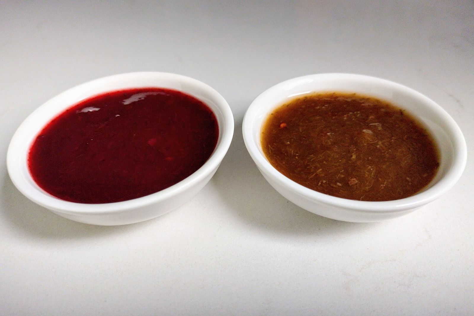 Two small bowls of tkemali plum sauce, one red and one brown