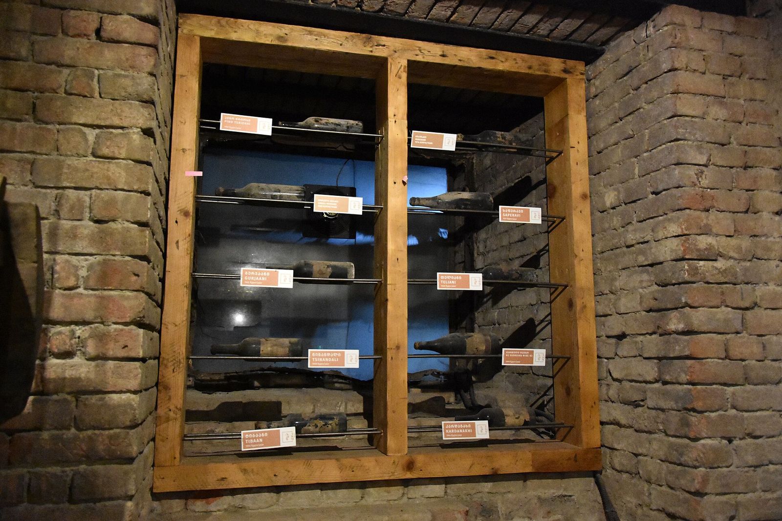Old bottles labeled Tsinandali, Saperavi, Gurjaani, Teliani and Kardanakhi on racks in a brick cellar at the Tbilisi Wine Museum