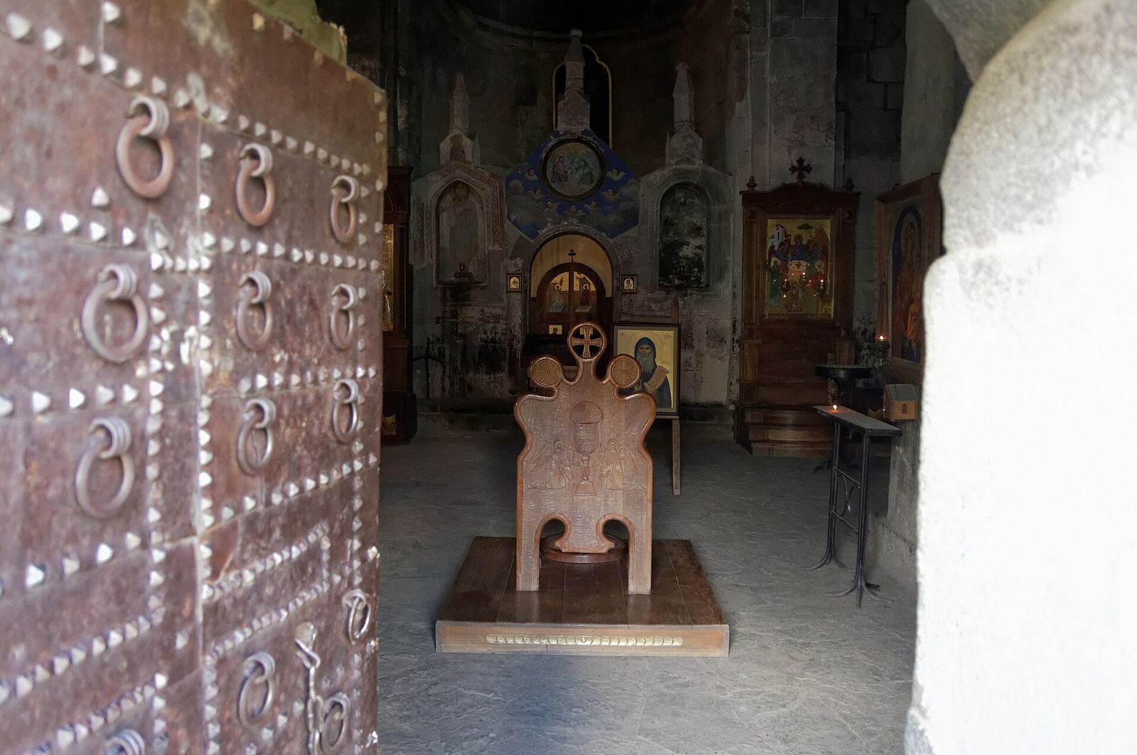 The dim interior of Gergeti Trinity Church seen through its studded iron door, with icons on the walls