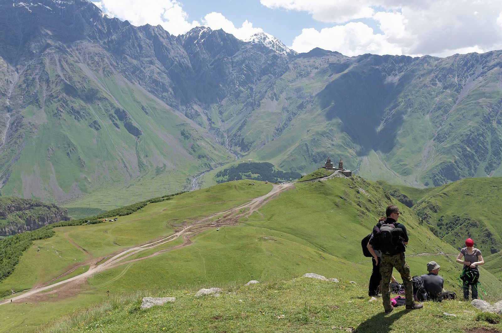 Hikers on the ridge above Gergeti Trinity Church looking down on the church on its hill, with the valley and the Kuro range behind