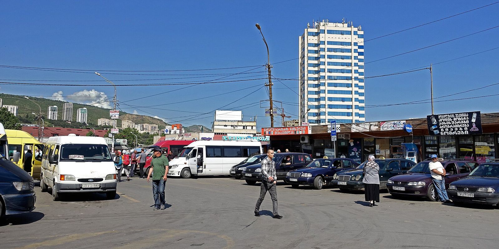 Marshrutka vans and waiting taxis at Didube bus station in Tbilisi, with a Kazbegi destination sign on a pole