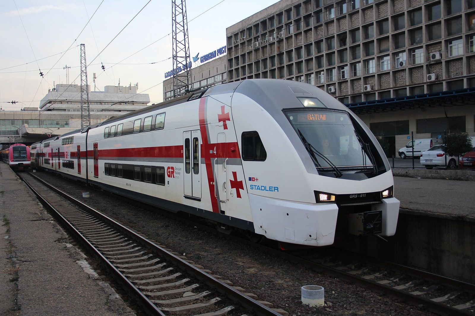 A red and white Georgian Railways Stadler double-deck train at a platform in Tbilisi Central Station