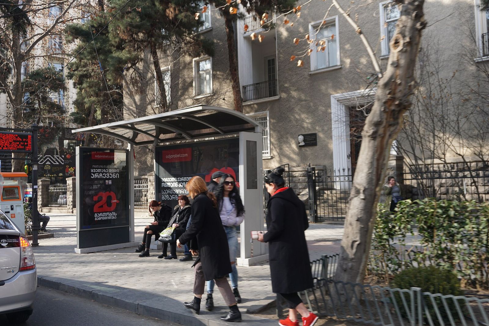 A bus shelter on Ilia Chavchavadze Avenue in Tbilisi with an electronic arrivals board on the left and people waiting