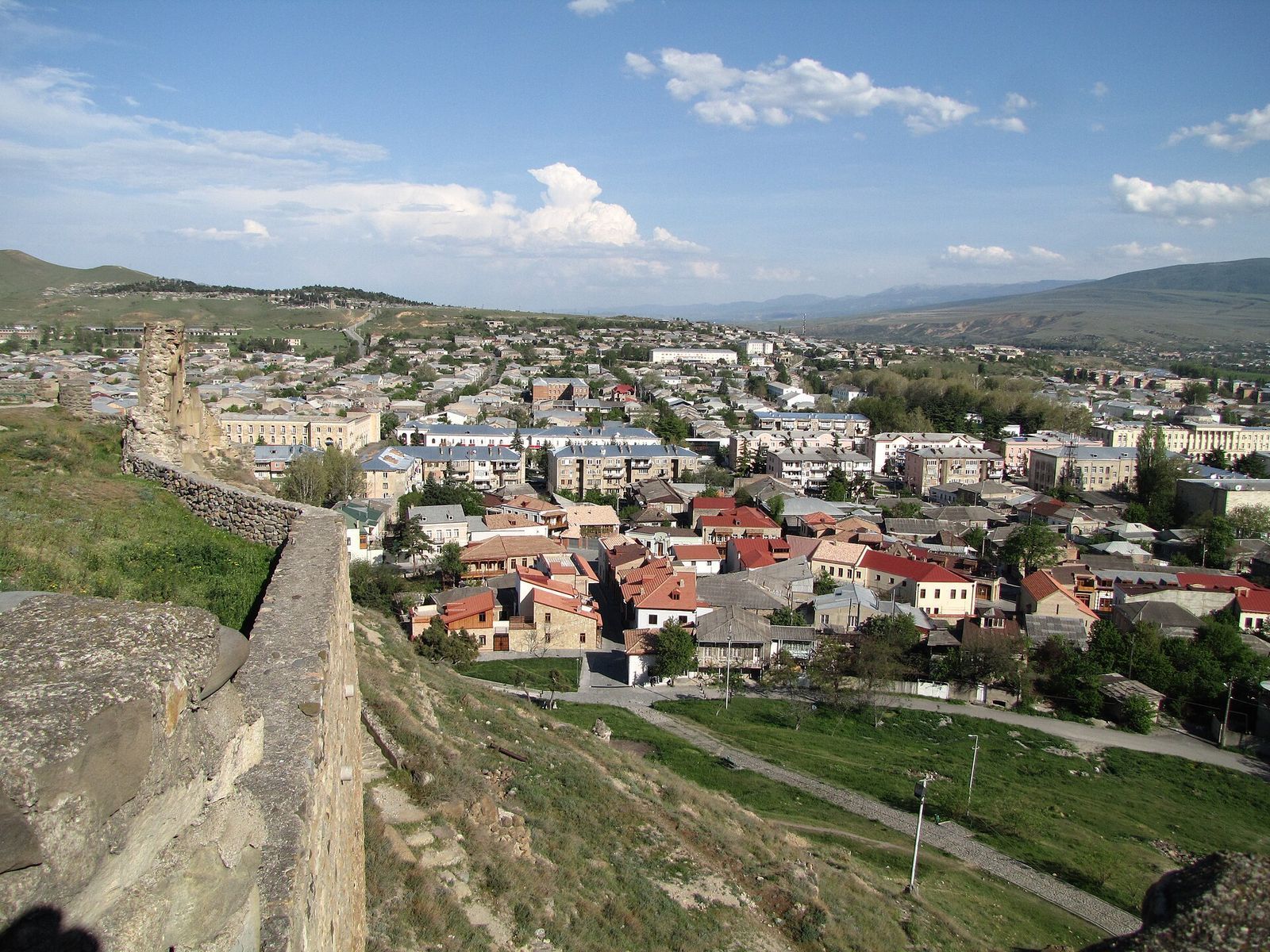 The rooftops and apartment blocks of Gori seen from the stone walls of Gori Fortress, with green hills beyond the town