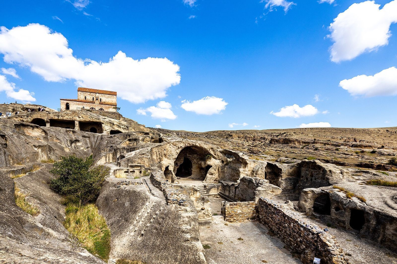 The rock-cut halls and streets of Uplistsikhe cave town spread over a sandstone ridge, with the brick church on the top