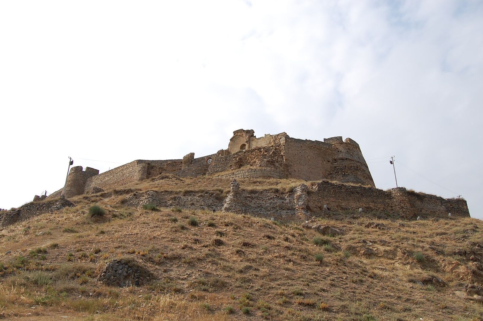 The stone walls and towers of Gori Fortress on its dry, grassy hill, seen from below