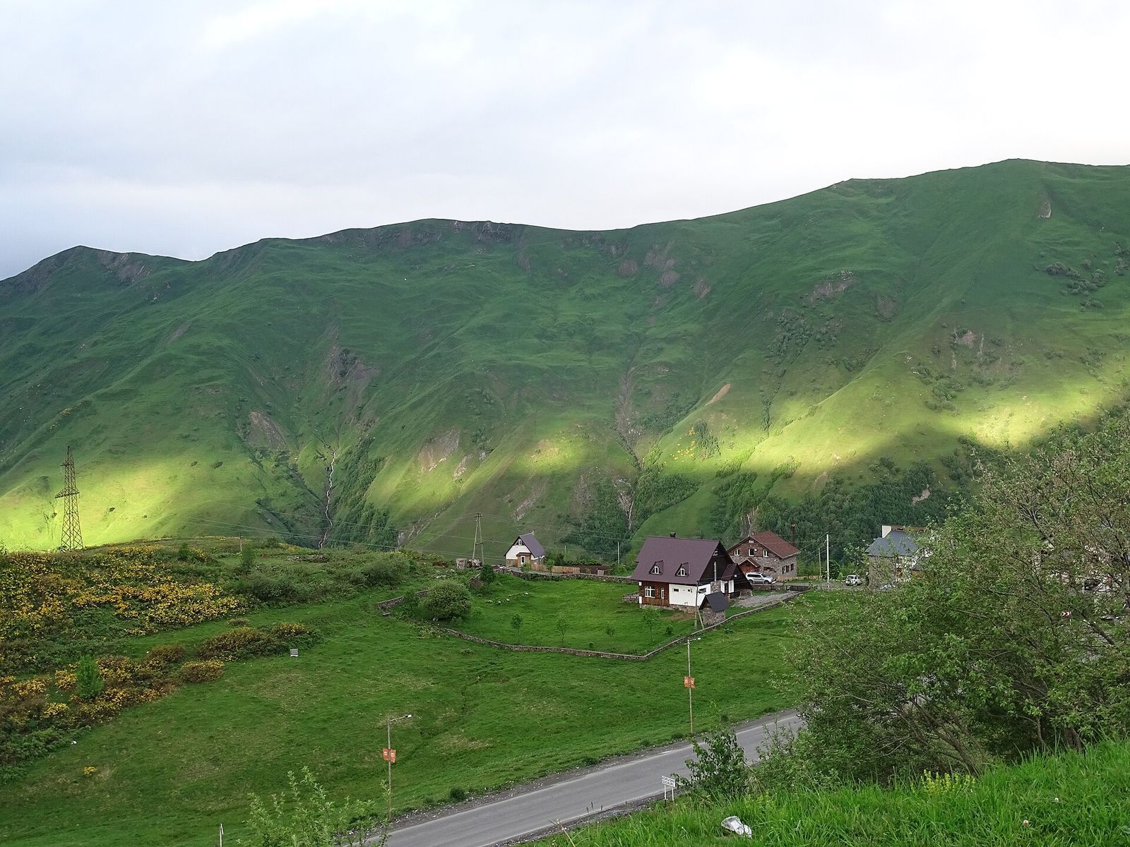 Green summer slopes above Gudauri with a few chalets beside the mountain road