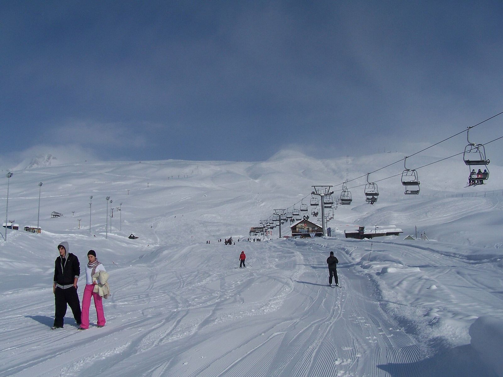 Skiers on a groomed piste in Gudauri with a chairlift climbing across the snow toward the upper slopes