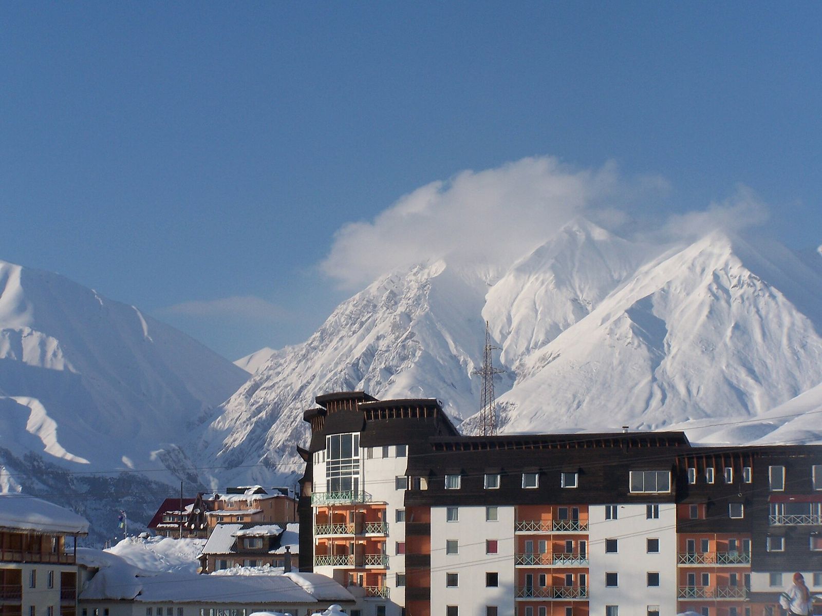 Gudauri hotel blocks with snow on the roofs and snow-covered Caucasus peaks behind