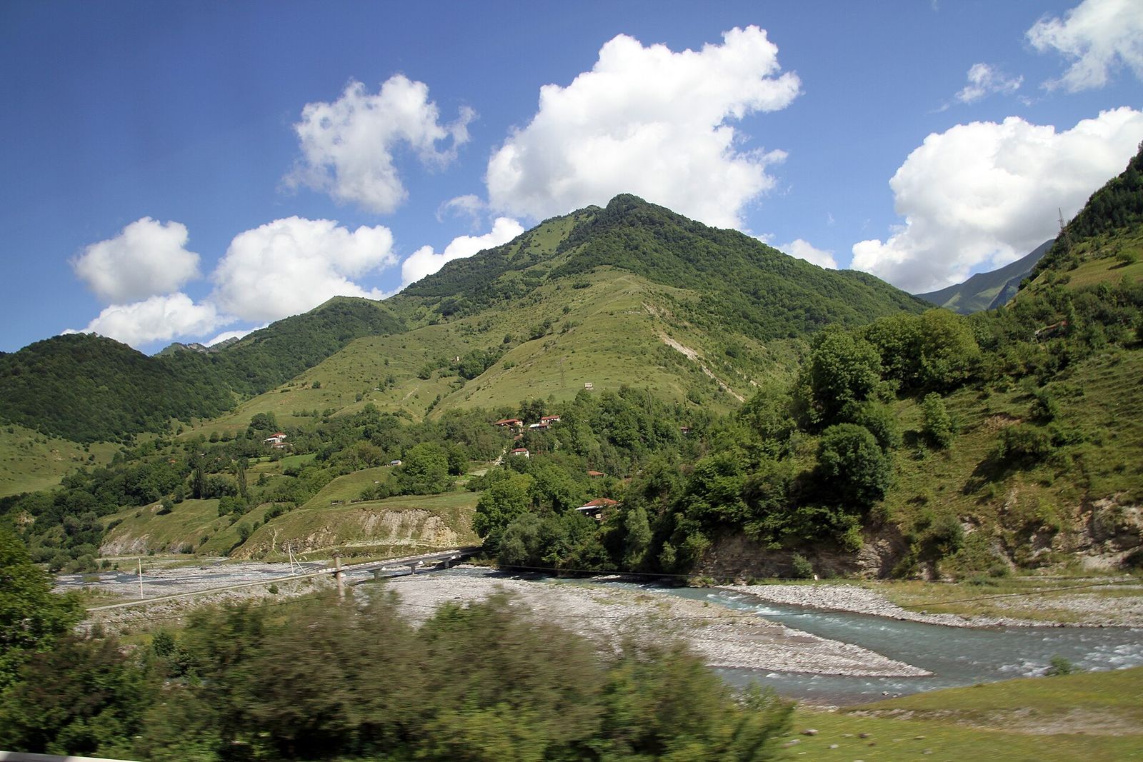 The Aragvi river running over a wide gravel bed below green mountains along the Georgian Military Highway