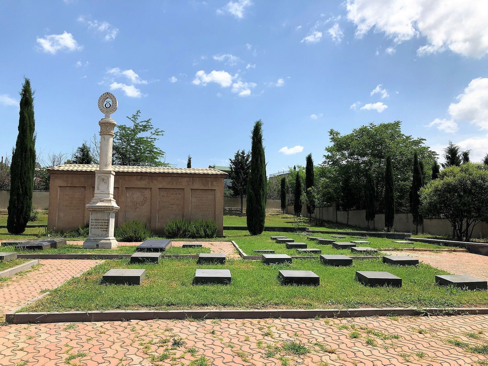 The Armenian Pantheon at Khojavank, with rows of dark gravestones, a white memorial column and cypress trees