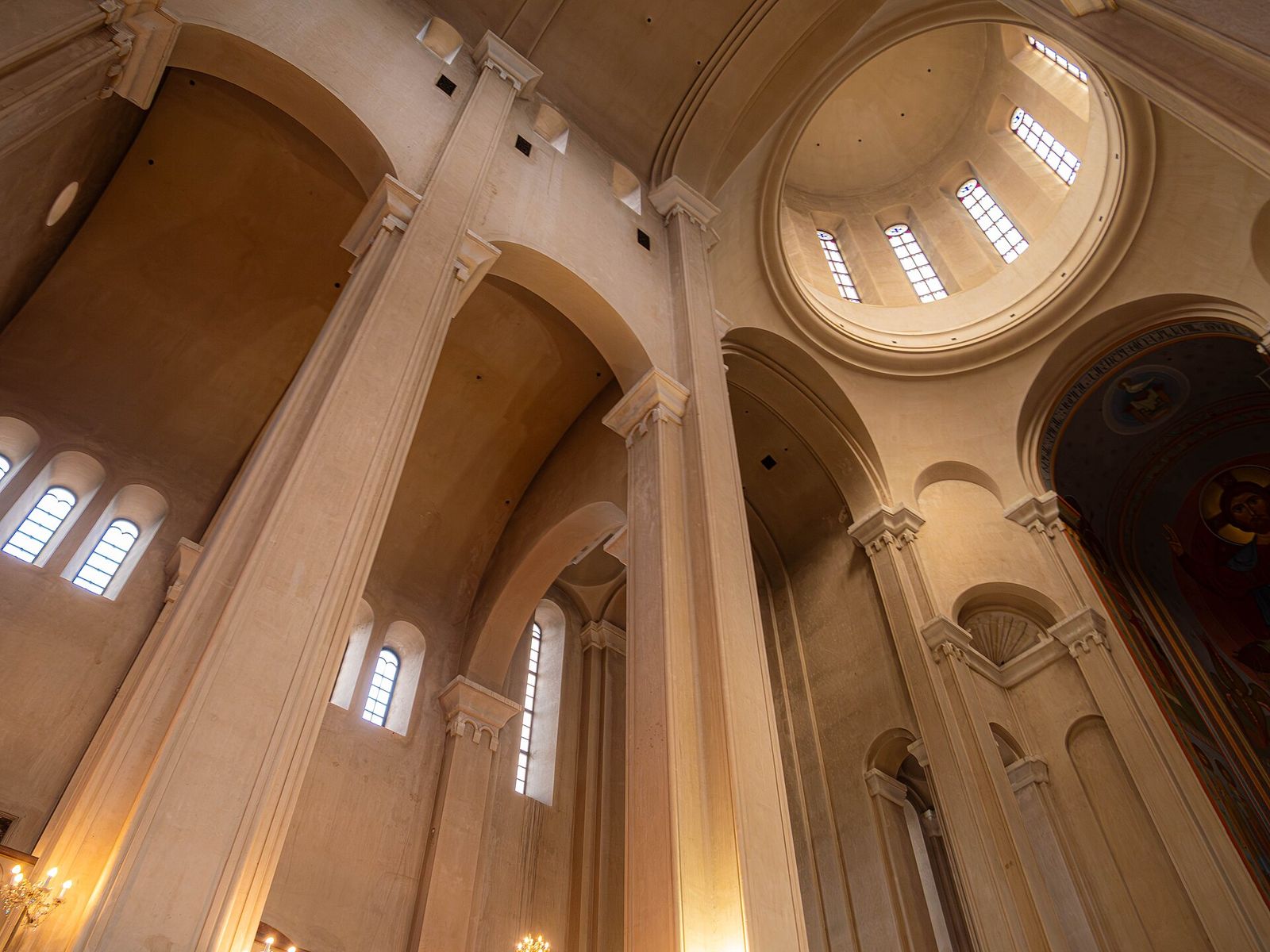 Looking up inside Sameba Cathedral at the tall stone columns, arched windows and the ring of windows in the dome
