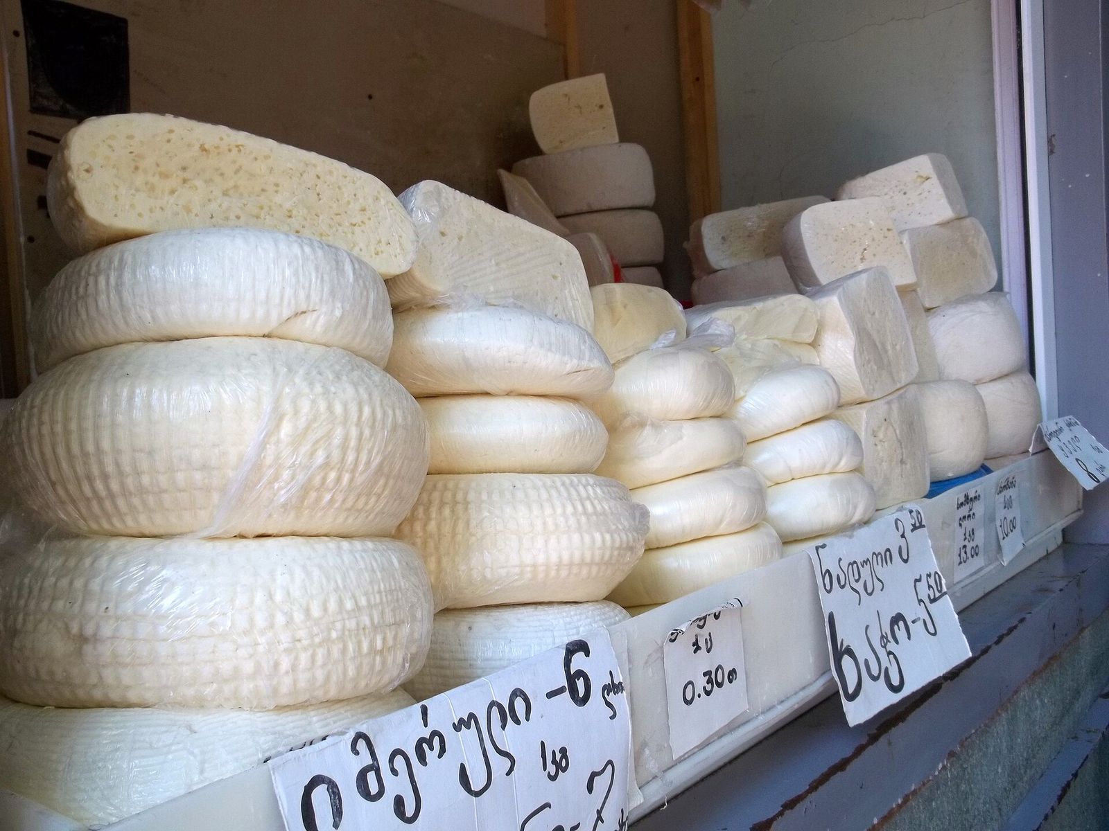 Wheels of imeruli and nadughi cheese with handwritten price signs at a Tbilisi cheese counter