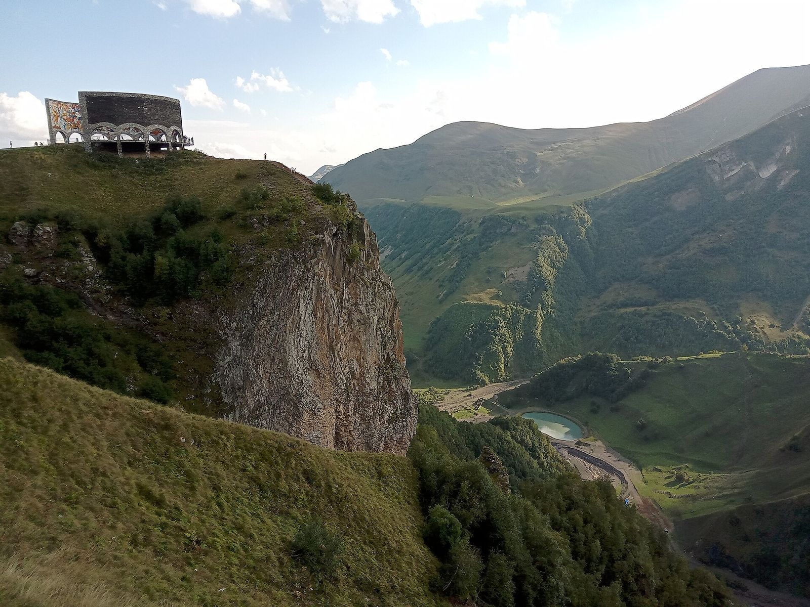 The Russia-Georgia Friendship Monument on a cliff edge above a green valley near the Jvari Pass