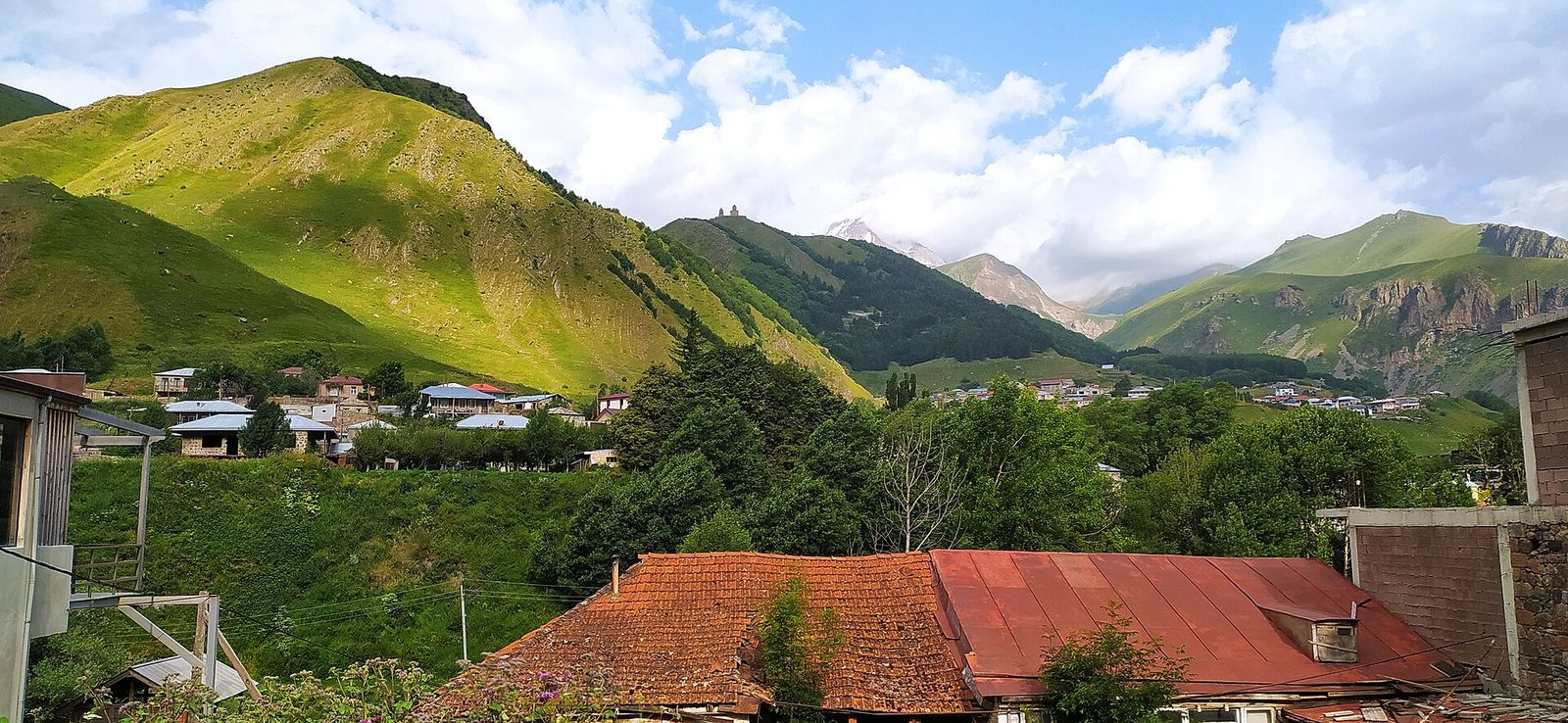 Rooftops of Stepantsminda with Gergeti village and green mountain slopes beyond