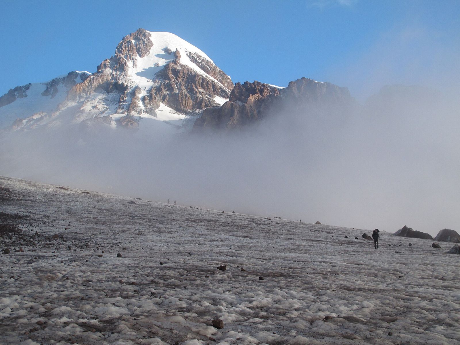 A hiker crossing the Gergeti Glacier below the snowy summit of Mount Kazbek