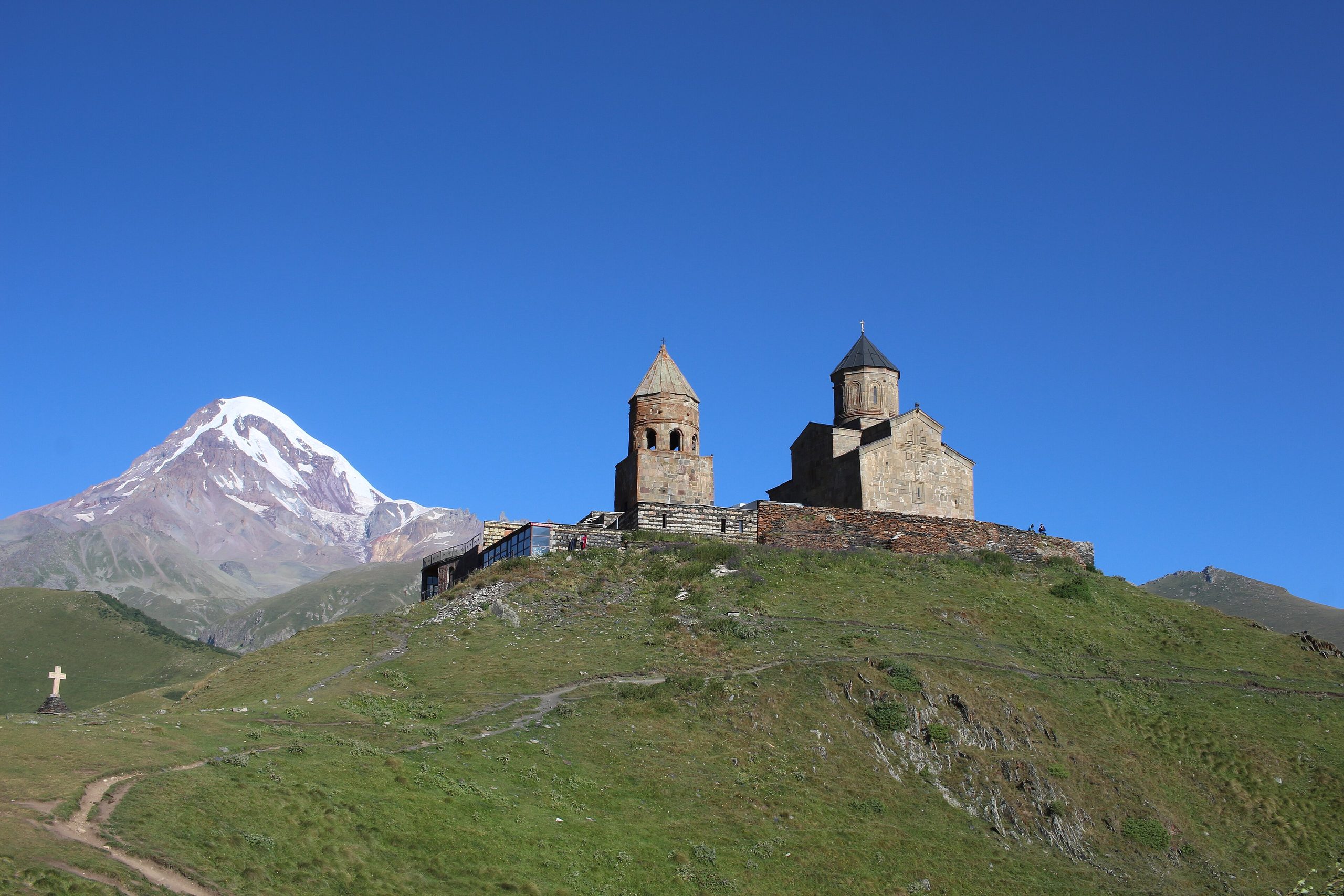 Gergeti Trinity Church on a green ridge with snow-capped Mount Kazbek behind
